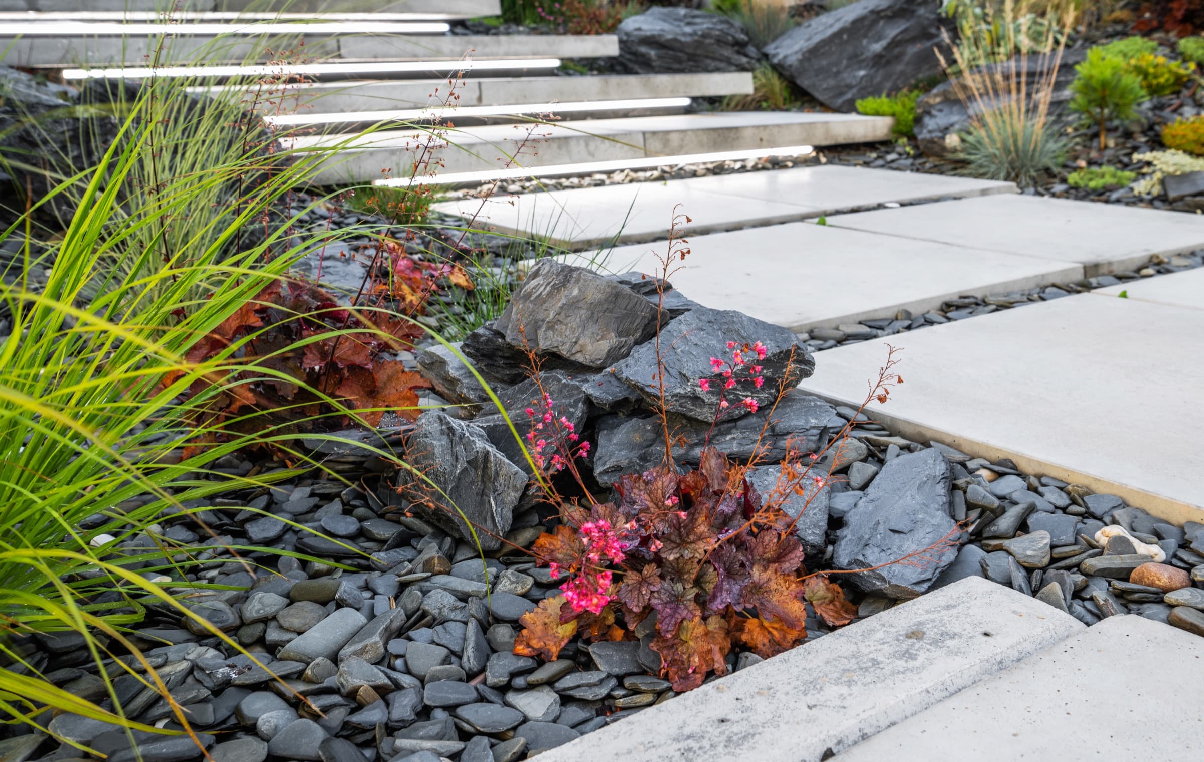 Contemporary garden with large-format paving, slate chippings, ornamental grasses and stone steps