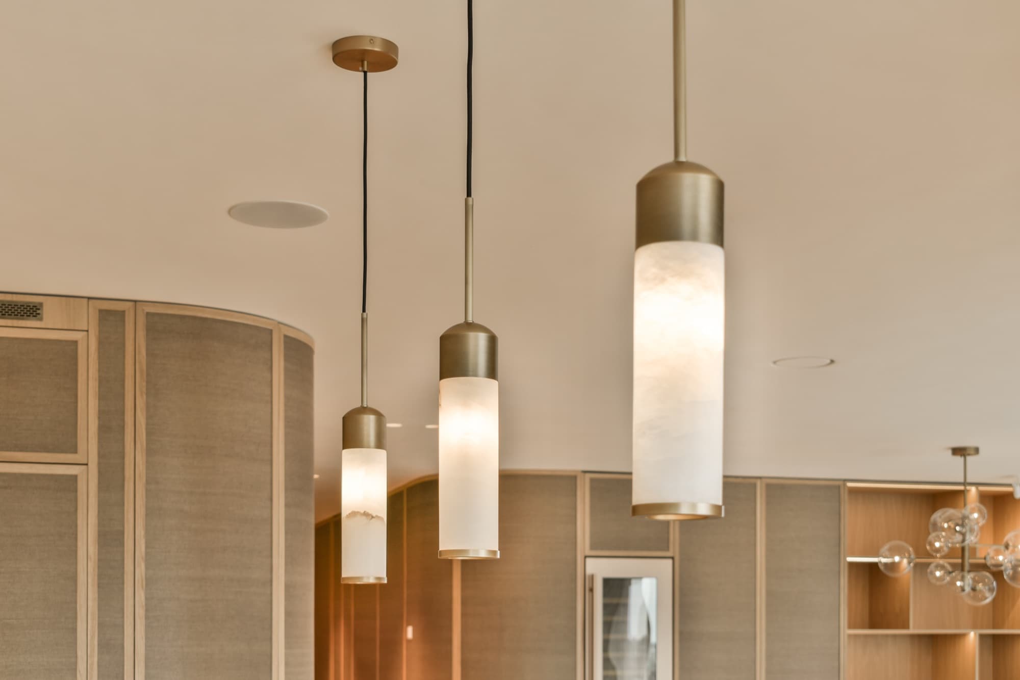 Brass and alabaster cylinder pendants lit above a fitted interior, with recessed downlights above